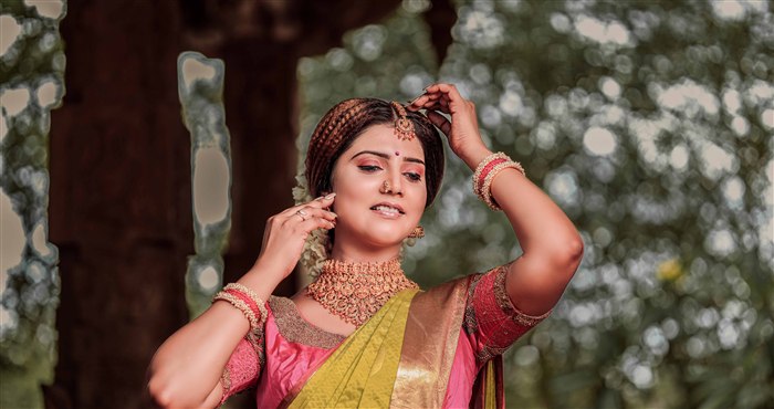 Bridal close-up portrait in pink saree with gold jewellery at a heritage temple pillar, bridal makeup by Ashvi Beauty Care, Jaffna