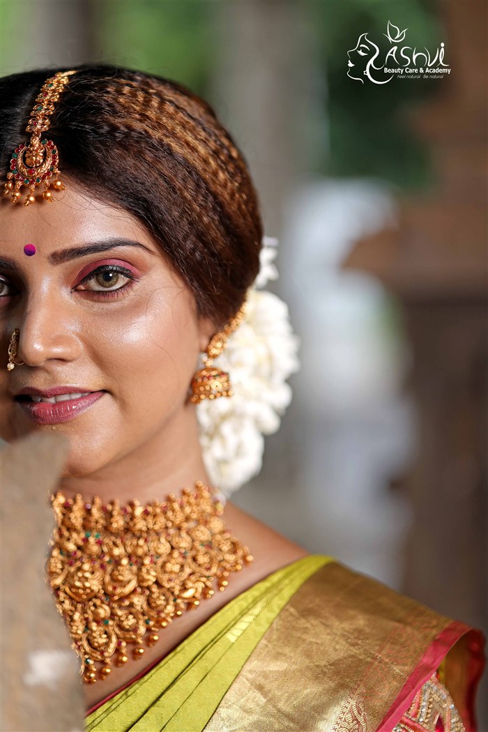Close-up bridal portrait with gold choker necklace and floral hair accent among palm leaves, Ashvi Beauty Care Jaffna
