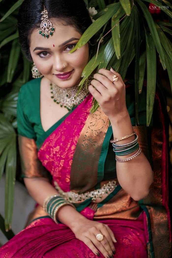 Smiling bride in pink and green silk saree seated among palm leaves, Ashvi Beauty Care Jaffna