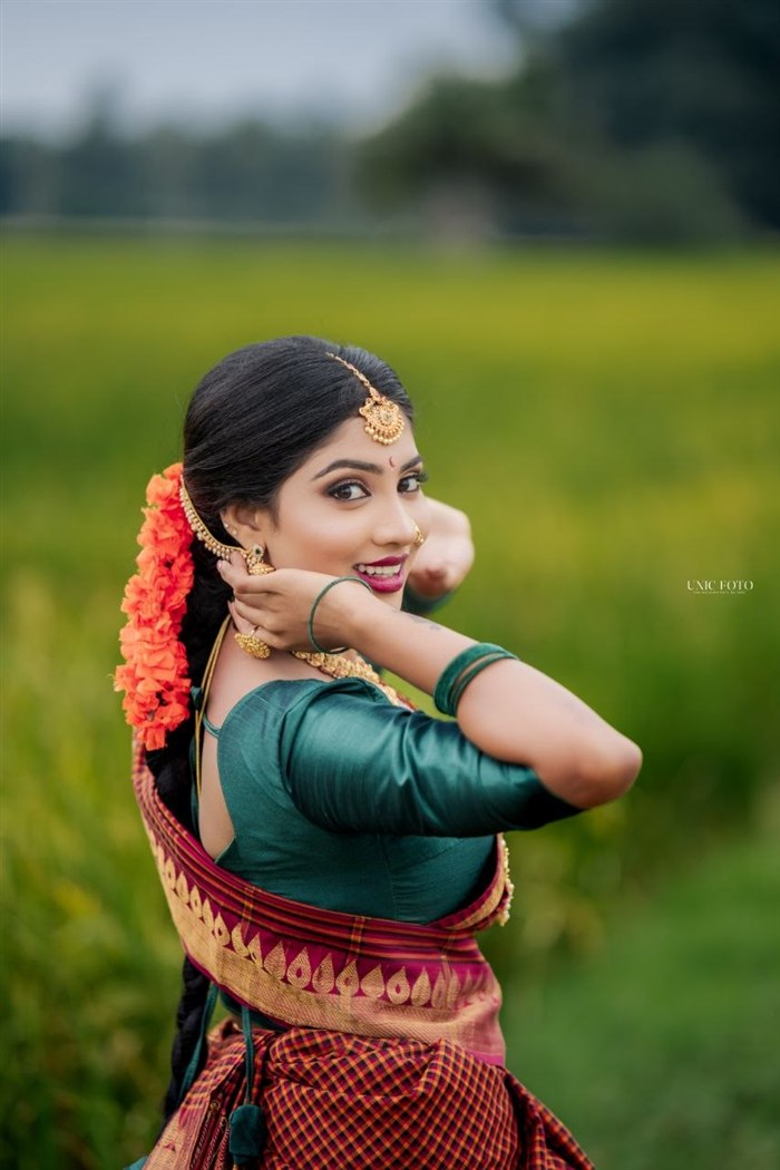 Bride in green silk saree with orange floral garland turning gracefully in a paddy field, Ashvi Beauty Care Jaffna