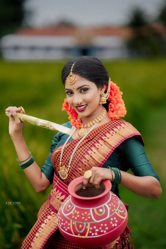 Smiling bride in maroon check saree holding sugarcane and a clay pot in a paddy field, Ashvi Beauty Care Jaffna