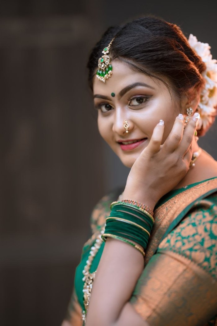 Bridal side-profile close-up in green and gold Kanjivaram saree with emerald jewellery, hand near cheek, Ashvi Beauty Care Jaffna