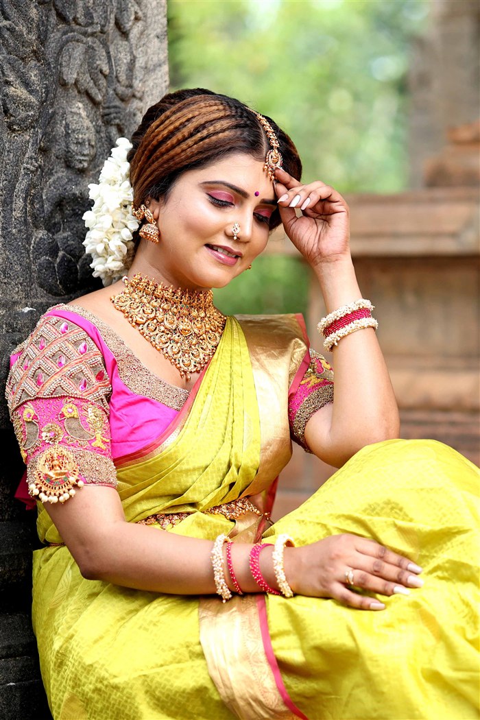 Bridal portrait in yellow and gold silk saree with temple jewellery, seated at temple steps, Ashvi Beauty Care Jaffna