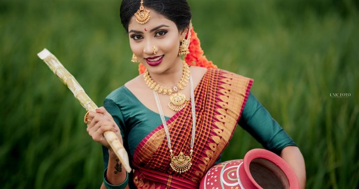Smiling bride in maroon check saree holding sugarcane and a clay pot in a paddy field, Ashvi Beauty Care Jaffna