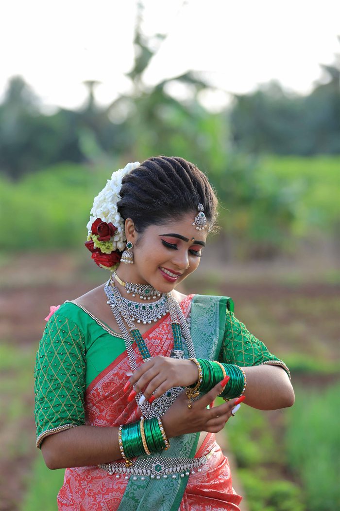 Candid bride adjusting green bangles in red and green saree, Ashvi Beauty Care Jaffna